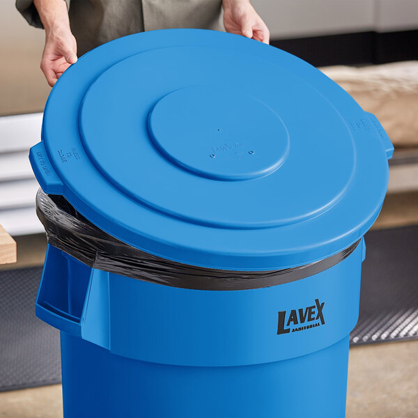 A woman holding a Lavex blue round commercial trash can lid.