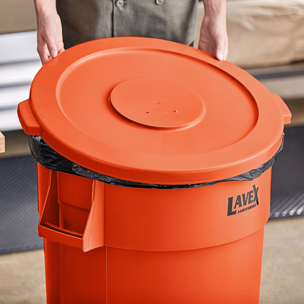 A person holding a large orange trash can lid.