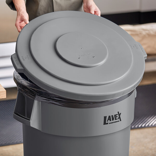 A person holding a Lavex gray round commercial trash can lid.