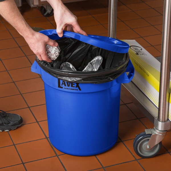A hand using a Lavex blue round lid to put foil in a blue trash can.