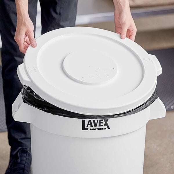 A person placing a Lavex white round lid on a trash can.