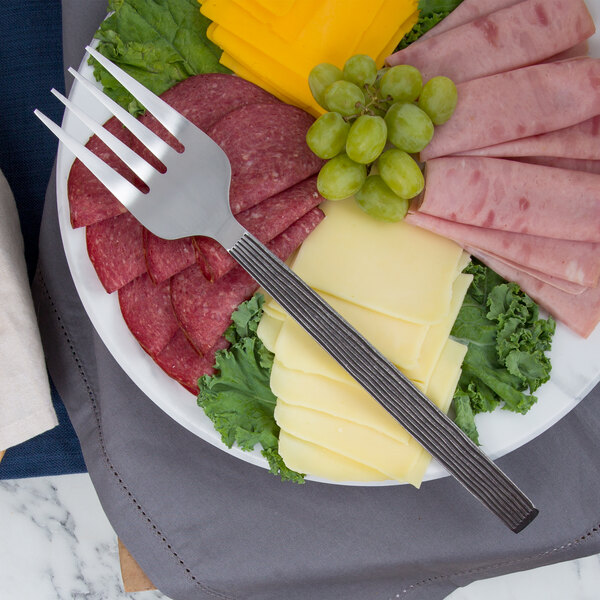 An American Metalcraft stainless steel cold meat fork on a plate of meat and cheese.