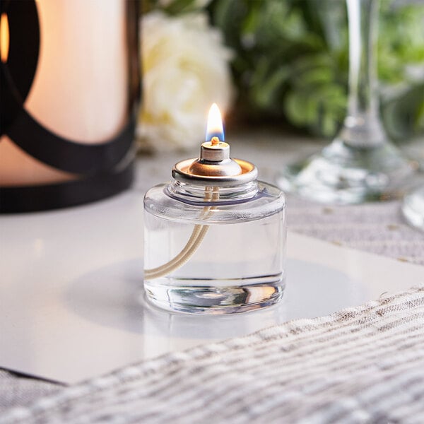 A Leola clear liquid wax candle burning in a glass bottle on a table.