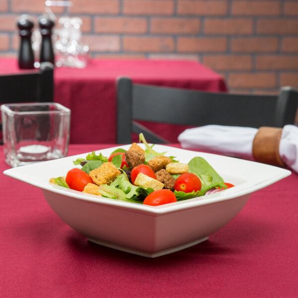 A Bone White porcelain bowl filled with salad on a table.