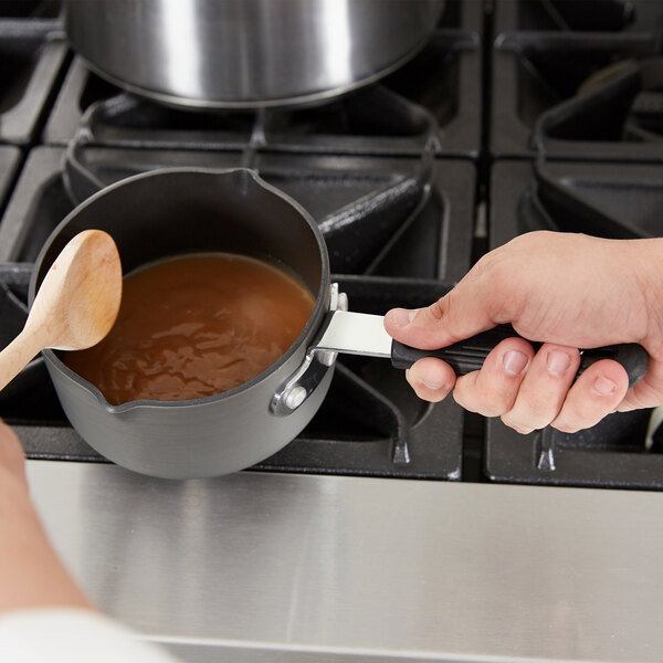 A person stirring a Thunder Group sauce pan with a wooden spoon.