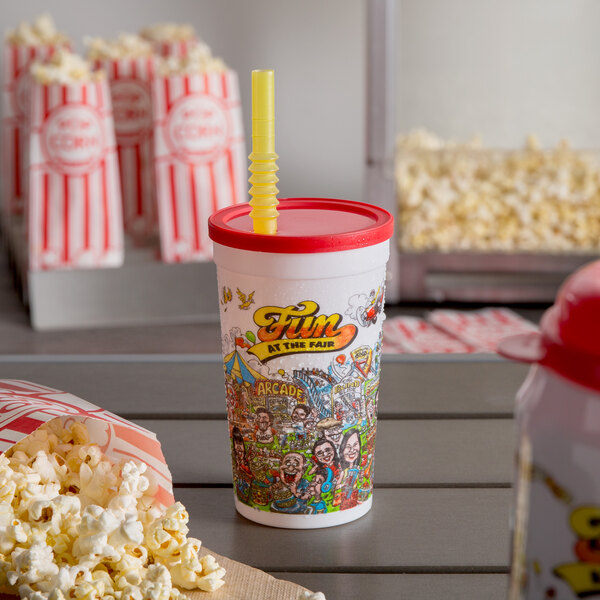 A white plastic cup with a red lid and a cartoon design on it next to a bag of popcorn.