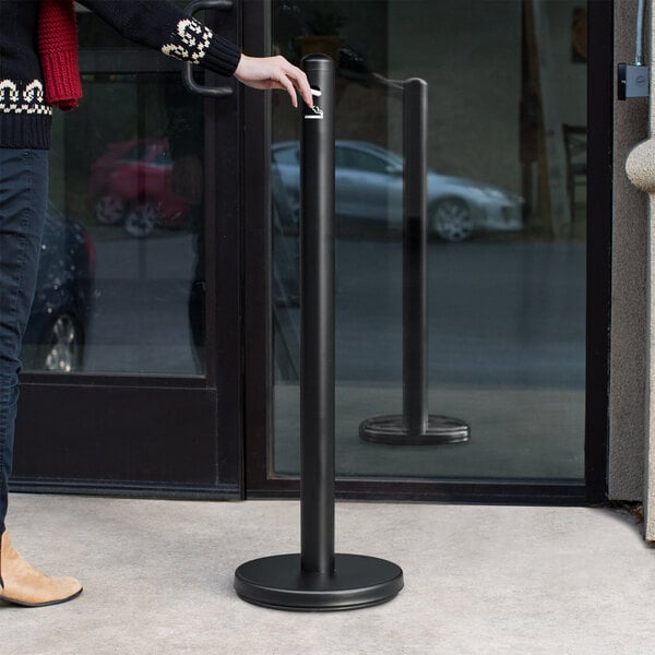 A person standing next to a Lavex black free standing smoker pole in front of a glass door.