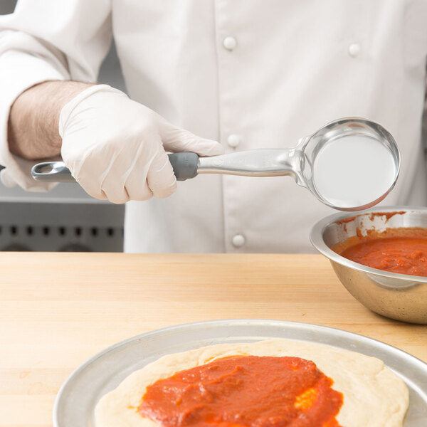 A person using a Vollrath Jacob's Pride Spoodle to serve sauce on a pizza.
