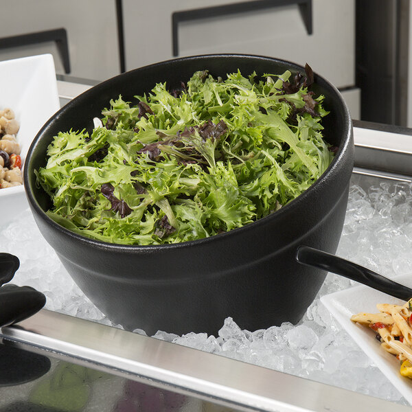A G.E.T. Enterprises Bugambilia black resin-coated aluminum bowl filled with green salad on a counter.