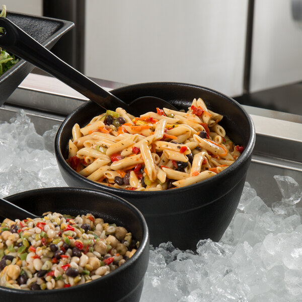 A black G.E.T. Enterprises Bugambilia round metal bowl filled with pasta and salad on a counter.