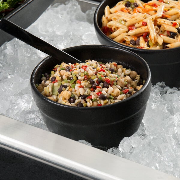 Two G.E.T. Enterprises Bugambilia black resin-coated aluminum bowls of food on ice with spoons and forks.