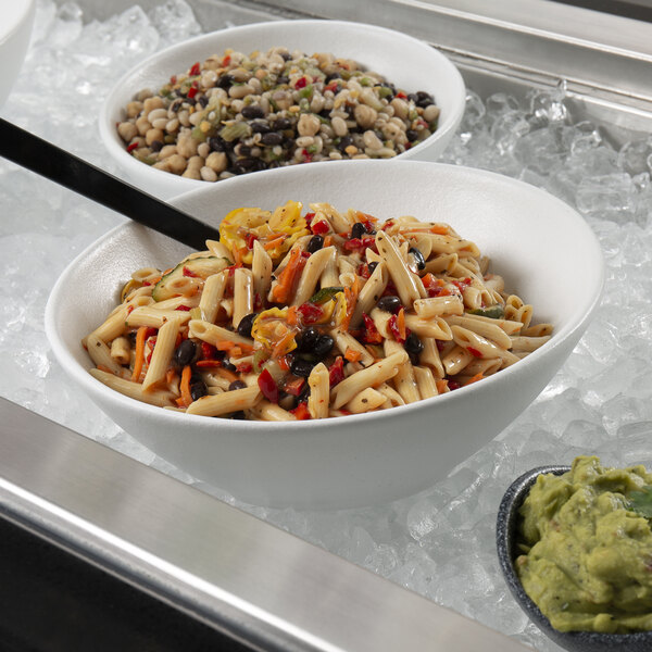 A white G.E.T. Enterprises resin-coated aluminum bowl filled with pasta and vegetables on a counter.