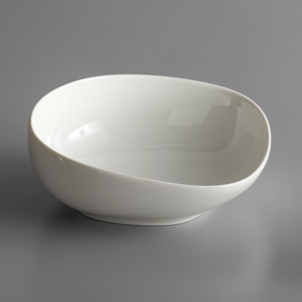 A Schonwald WellCome cream porcelain salad bowl with a curved edge on a gray surface.