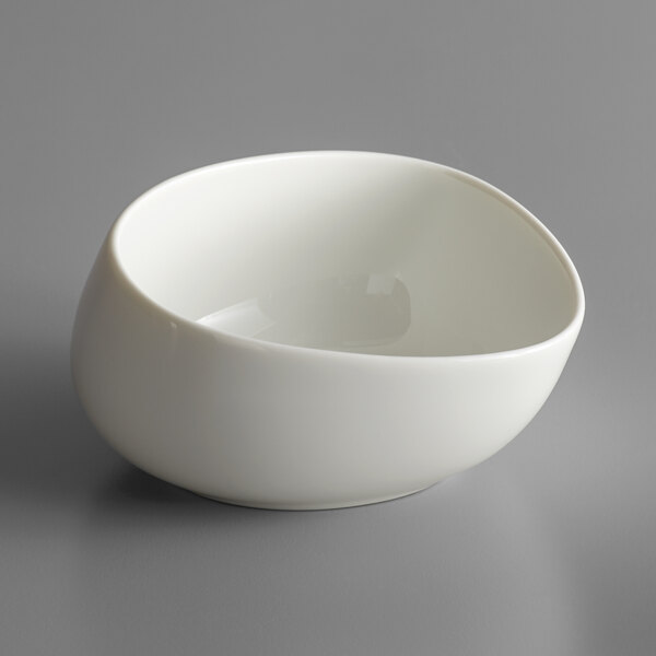 A white Schonwald organic bowl with a curved edge on a gray surface.