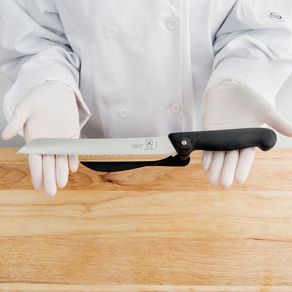 A person using a MercerSlice serrated knife to slice bread on a wooden table.