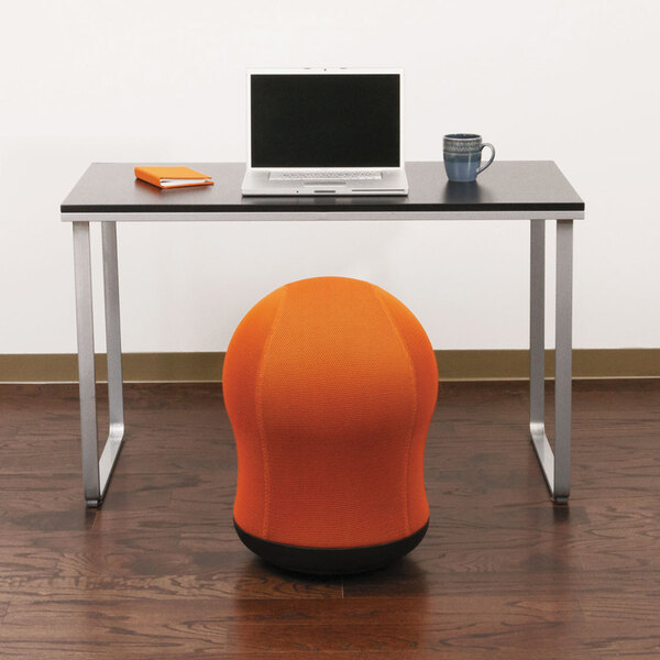 An orange Safco Zenergy ball chair in front of a desk with a laptop.