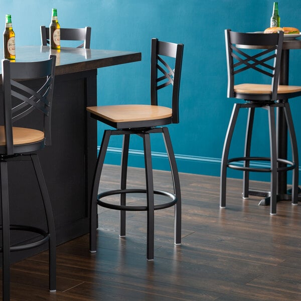 A Lancaster Table & Seating black cross back swivel bar stool with a natural wood seat.