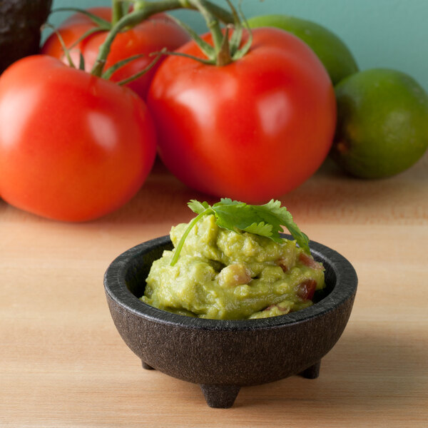 A charcoal polypropylene pequeno molcajete filled with guacamole and tomatoes.
