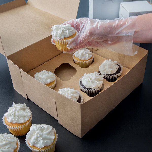 A hand placing a cupcake with white frosting into a Kraft cupcake box with a 6 slot insert.
