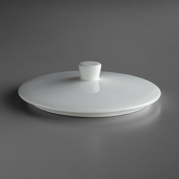 A Schonwald bone white porcelain bowl lid with a small knob on top on a white plate.