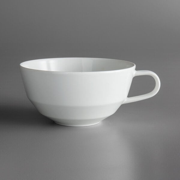 A close up of a Schonwald Allure bone white cup with a handle on a gray surface.