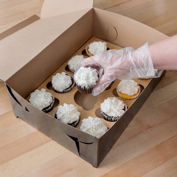 A hand holds a Baker's Mark black cupcake box with a white frosted cupcake inside.