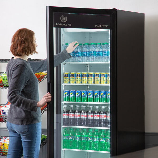 A woman opening a Beverage-Air Marketeer refrigerator with bottles of soda.