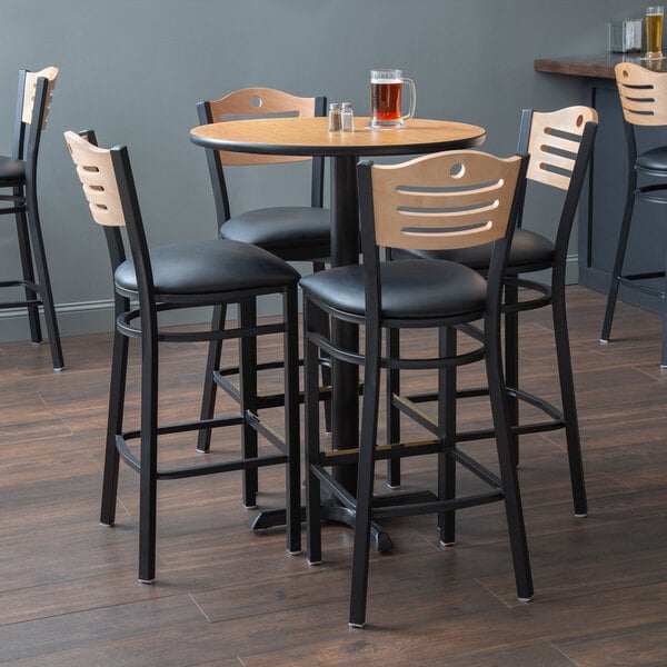 A Lancaster Table & Seating bar height dining set with a table with a glass of beer and chairs with black padded seats.