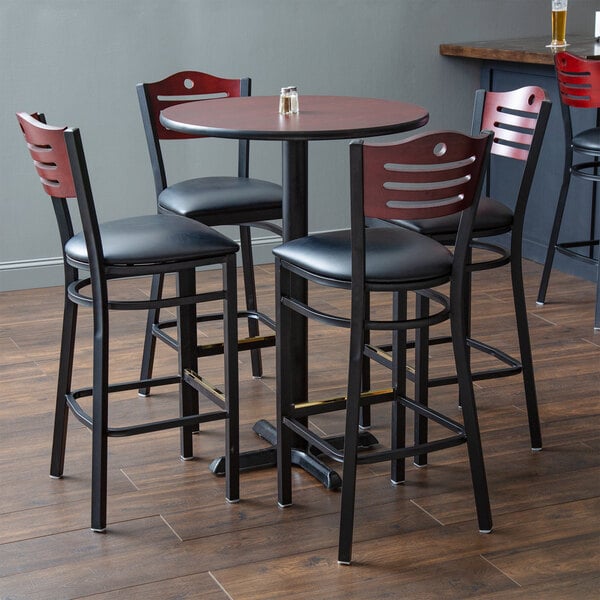 A Lancaster Table & Seating bar height table with black chairs and padded seats.
