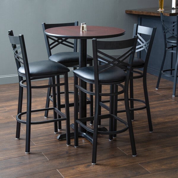 A Lancaster Table & Seating bar table with black chairs and black padded seats.