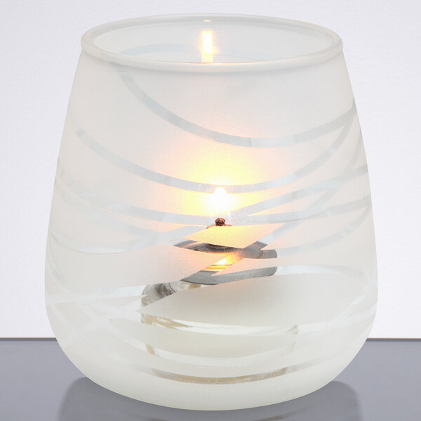 A Sterno Fiano votive with a lit white candle inside on a white plate.