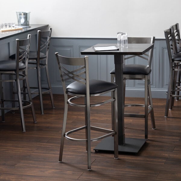 A Lancaster Table & Seating live edge bar height table with a black cushioned chair.