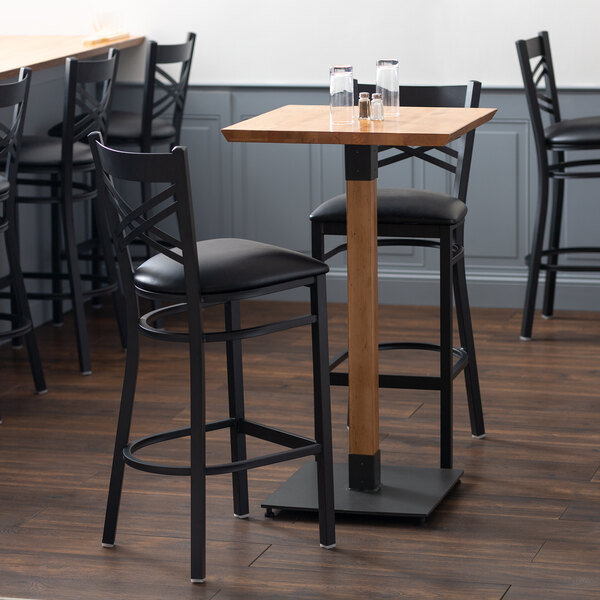 A Lancaster Table & Seating live edge bar height table with a wooden table top and black bar stools.