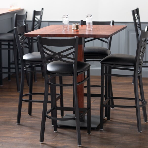 A Lancaster Table & Seating solid wood bar height table with mahogany finish and black bar stools around it.
