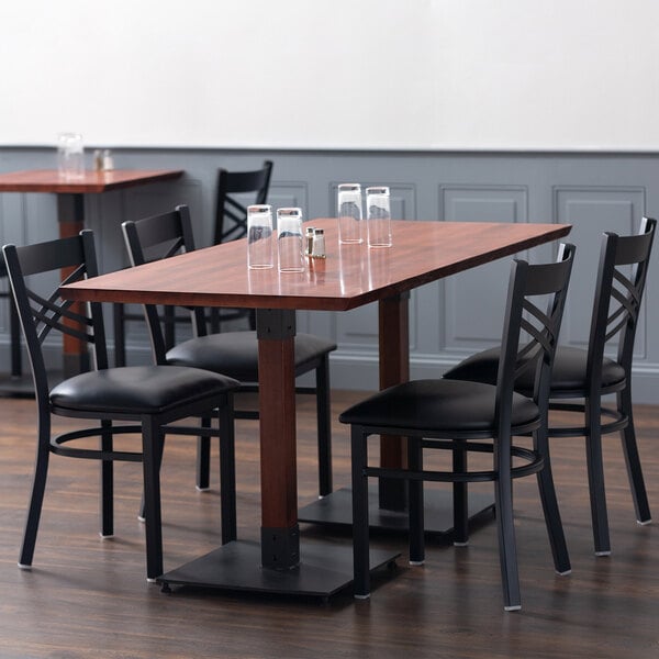 A Lancaster Table & Seating live edge dining table with mahogany finish and black chairs with glasses on it.