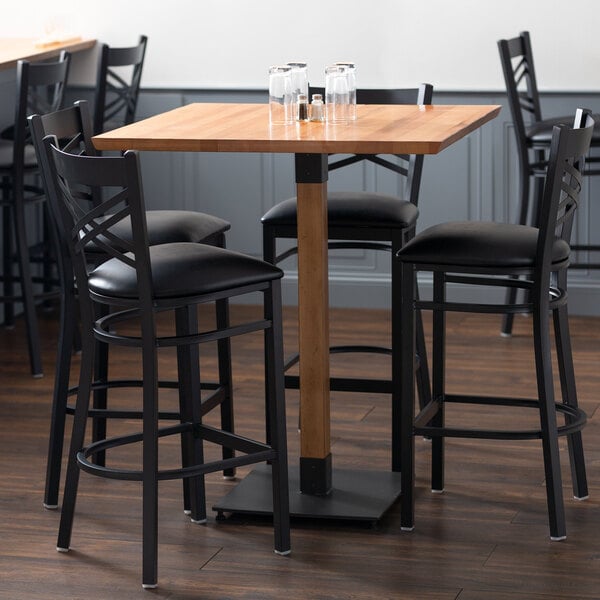 A Lancaster Table & Seating wooden table with black bar stools around it.
