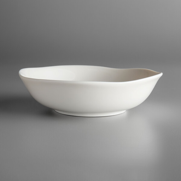 A white Oneida Lancaster Garden porcelain bowl with a curved edge on a grey surface.