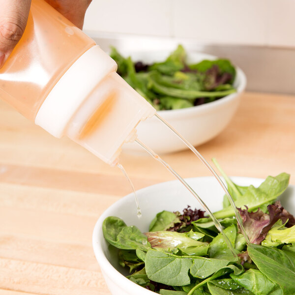 A hand pouring liquid from a Tablecraft SelecTop squeeze bottle into a bowl of salad.