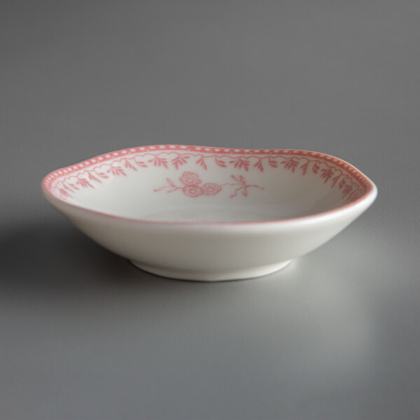 A white porcelain sauce dish with pink writing on it.