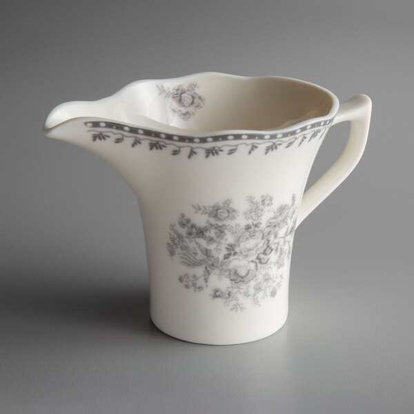 A white and grey porcelain creamer with a floral design and handle.