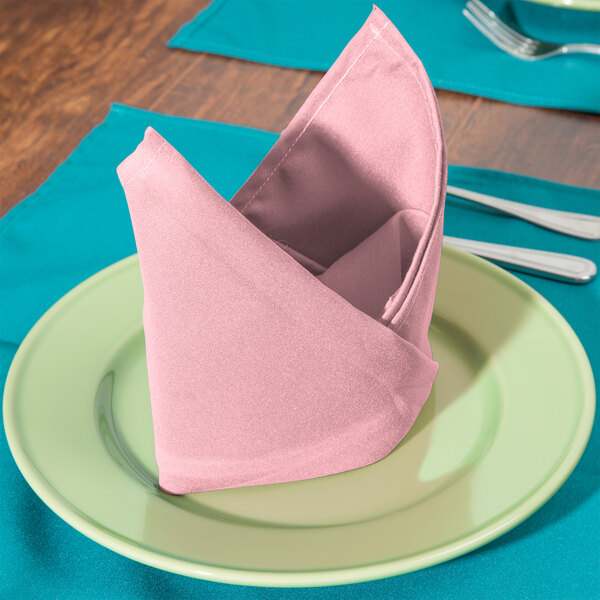 A folded pink Intedge cloth napkin on a plate with silverware.