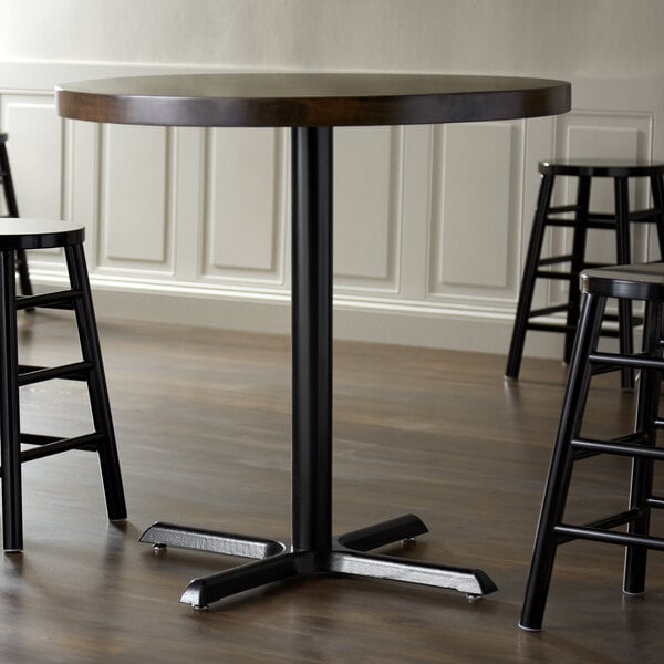A Lancaster Table & Seating black cast iron counter height table base with a round table and stools on it.