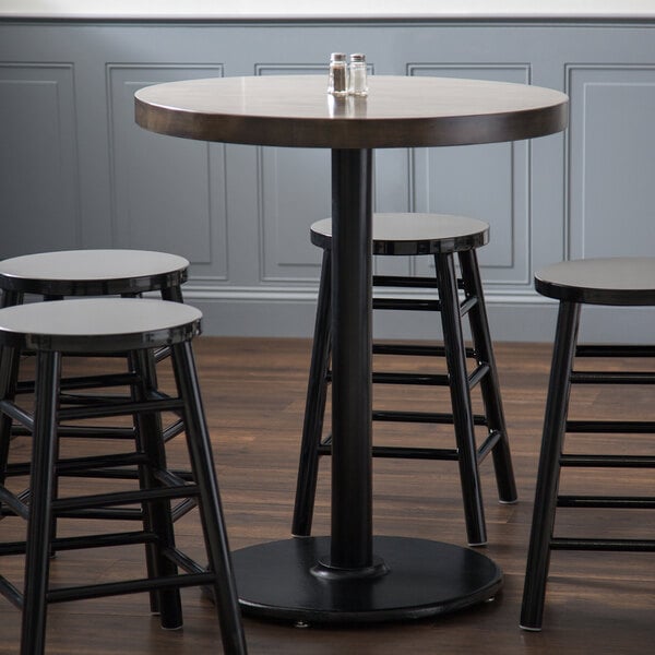 A Lancaster Table & Seating black cast iron round counter height table base with three stools around it.