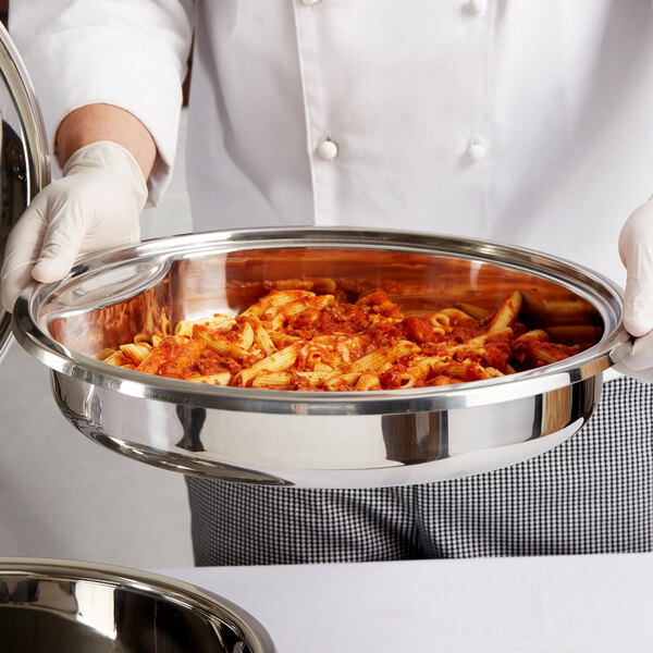 A person holding a Vollrath stainless steel food pan filled with pasta.