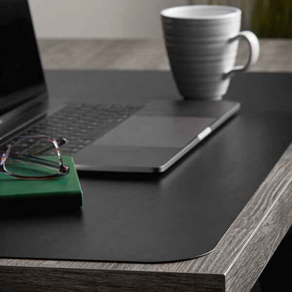 A black ES Robbins desk pad on a desk with a laptop and a mug.