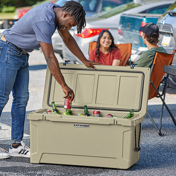 A man wearing a hat putting a can of beer into a tan CaterGator outdoor cooler.