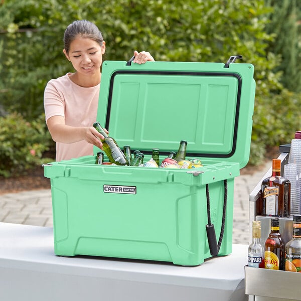 A woman putting bottles into a CaterGator Seafoam outdoor cooler.