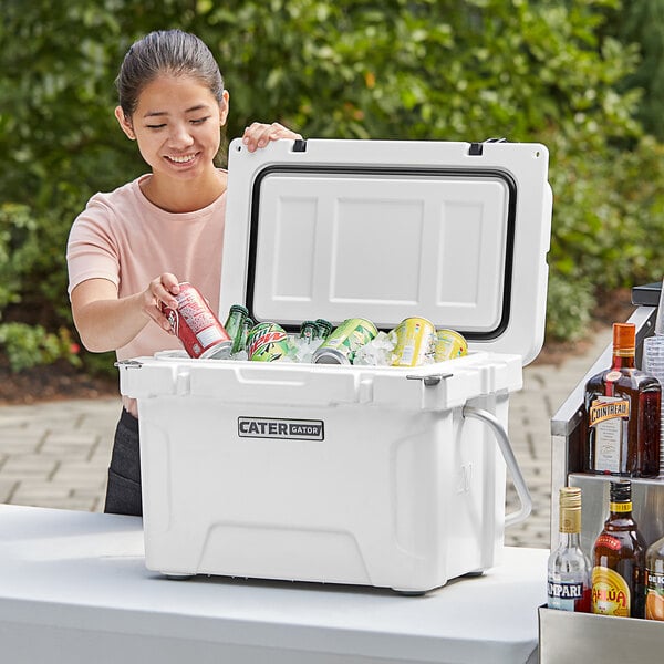 A woman opening a white CaterGator outdoor cooler to put red cans inside.