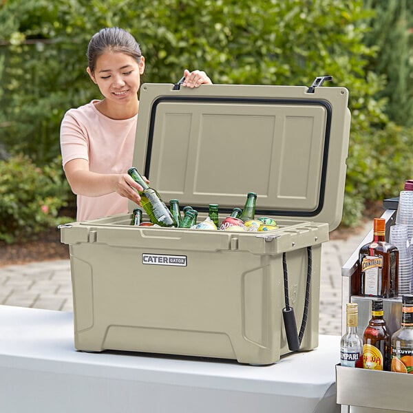 A woman putting bottles into a tan CaterGator outdoor cooler.