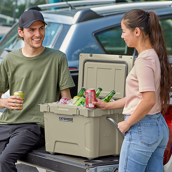 A man and woman standing next to a tan CaterGator outdoor cooler filled with beer and ice.
